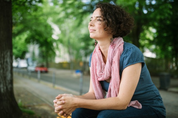 eine 30-jährige Frau sitzt im Park auf einer Bank.