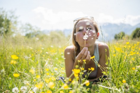 Junge Frau liegt auf Wiese und bläst in Pusteblume