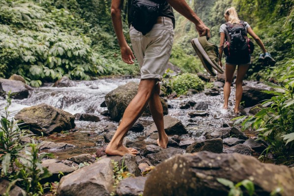 Ein junges Paar wandern barfuß auf den Steinen an einem Bach entlang.