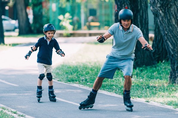 Ein Mann fährt mit seinem Sohn auf Inlineskates einen asphaltierten Weg entlang. beide tragen Helm und Armschoner.