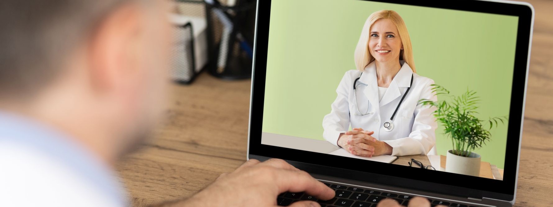 Ein Mann sitzt vor einem Laptop. Auf dem Bildschirm ist eine Ärztin, die eine Videosprechstunde gibt.