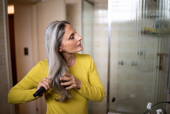 Ältere Frau kämmt ihre langen grauen Haare im Badezimmer