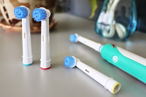 Türkisfarbene elektrische Zahnbürste und drei Wechselköpfe liegen auf Waschtisch.