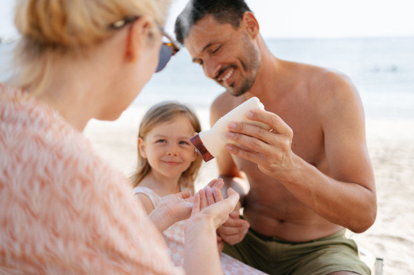 Familienvater drückt Sonnencreme aus der Flasche auf die hand seiner Frau