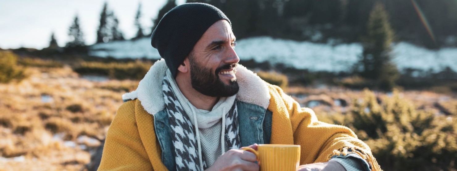 Ein etwa 35-jähriger Mann sitzt in der Natur und trinkt eine Tasse Tee. 