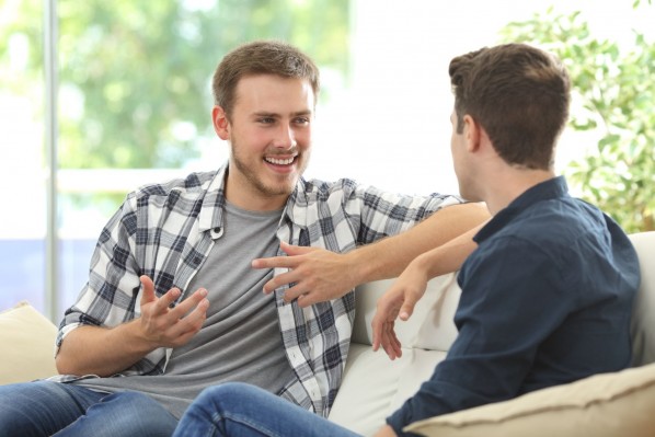 Zwei etwa 25 jährige Männer sitzen auf einem Sofa und unterhalten sich angeregt.