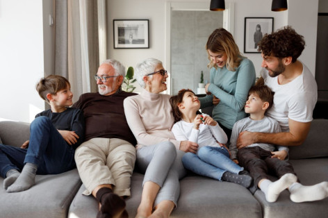 Eine 7-köpfige Familie mehrer Generationen sitzen gemeinsam auf einem Sofa und lachen.