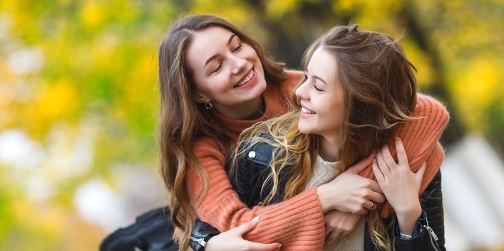 Zwei circa 16-jährige Freundinnen umarmen sich im Park.