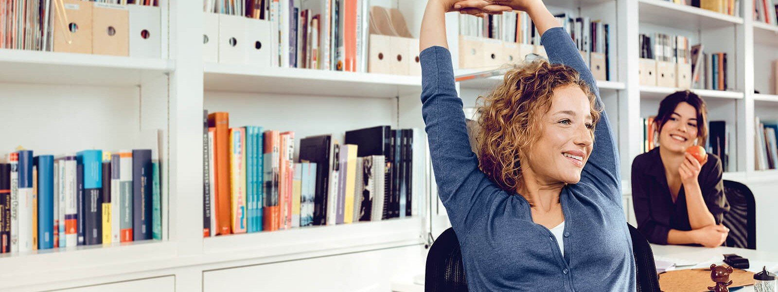 Eine Büroangestellte streckt sich auf ihrem Bürostuhl aus