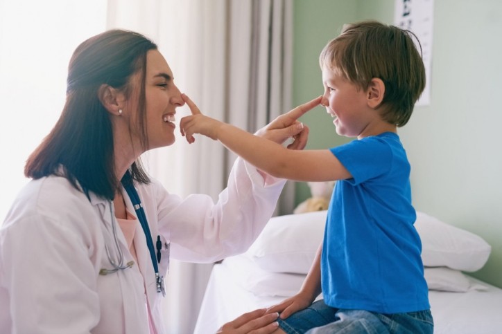 Eine Kinderärztin und ein etwa 3 jähriger Junge fassen sich gegenseitig an die Nasen und lächeln dabei.