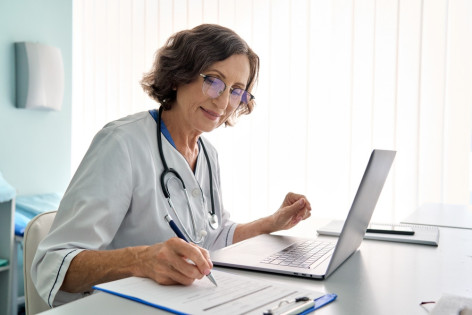 Eine Ärztin nimmt an dem Telemedizin-Netzwerk in Sachsen-Anhalt teil und macht sich Notizen vor ihrem Laptop.