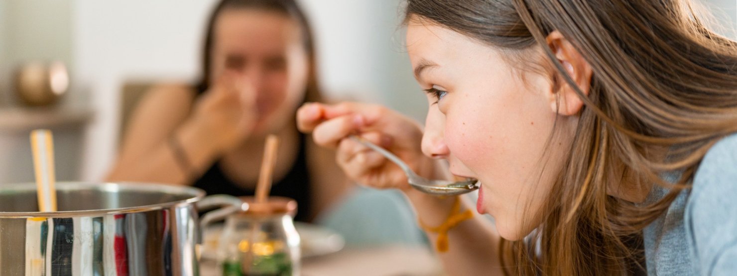 Zwei etwa 13-jährige Mädchen essen Suppe an einem Esstisch.