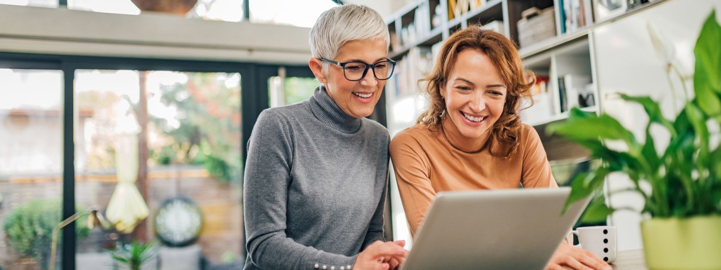 Zwei arbeitende Frauen sitzen zusammen am Tisch und schauen auf einen Laptop.