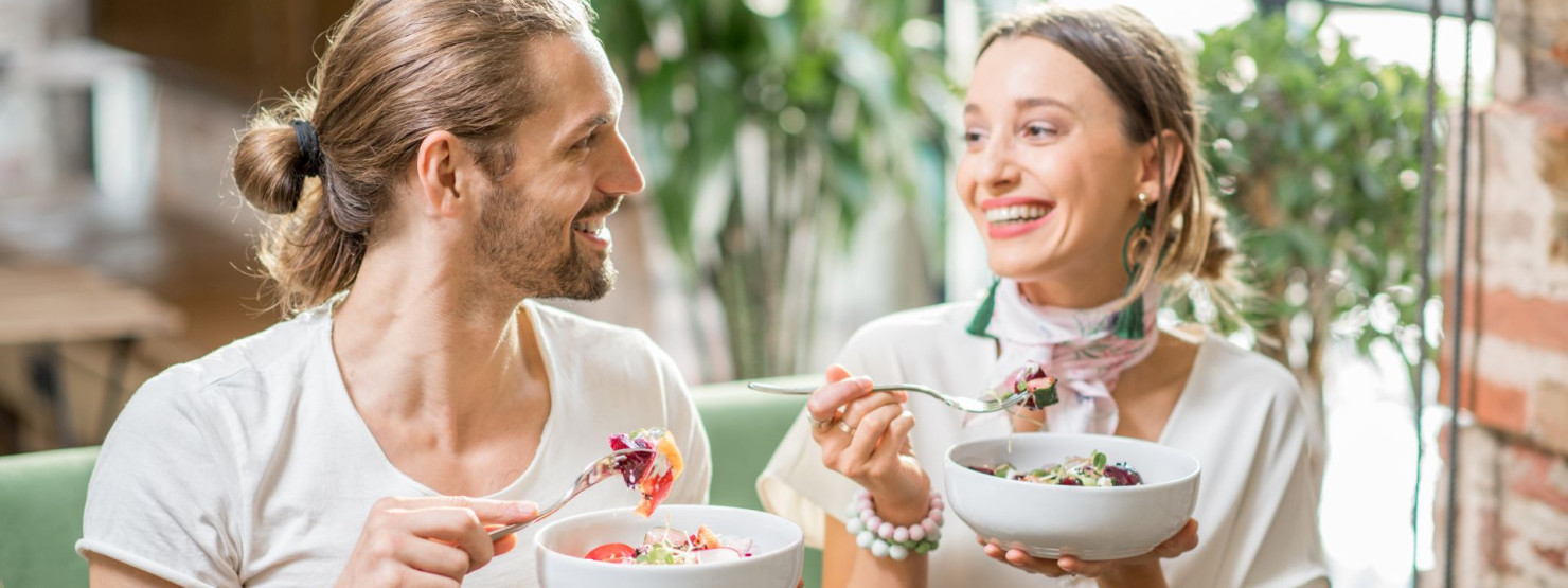 Zwei Arbeitskollegen unterhalten sich freudig während ihrer Mittagspause. In den Händen halten Sie volle Salatschüsseln.
