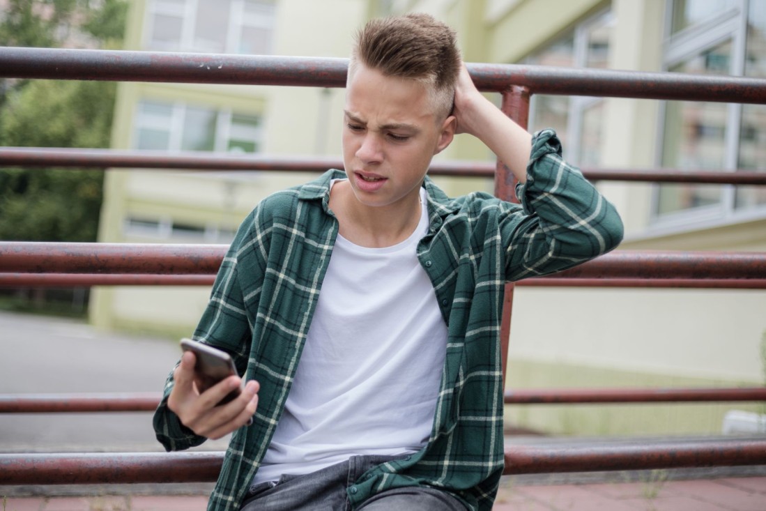 Ein Teenager schaut fragwürdig auf sein Smartphone und fasst sich dabei verwundert an seinen Kopf. 