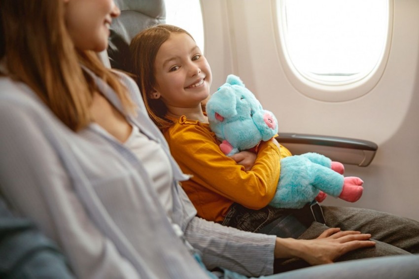 Cheerful child holding toy and smiling while traveling with mother in commercial aircraft