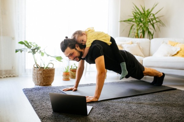 Kind liegt auf dem Rücken des Vaters. der Sportübungen vor dem Laptop macht.