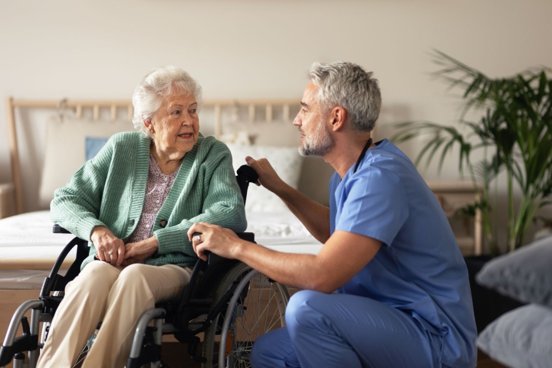 Ein Pfleger spricht mit einer Seniorin im Rollstuhl.