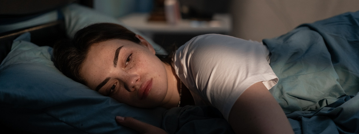 Eine etwa 25-jähriger Frau liegt nachts im Bett wach. Licht von draußen scheint in das Schlafzimmer und in ihr Gesicht.