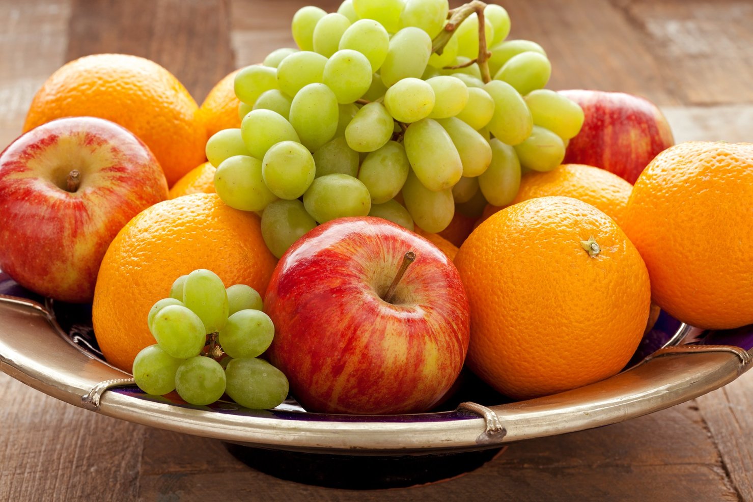 Eine Obstschale mit Weintrauben, Äpfeln und Orangen steht auf einem Tisch.