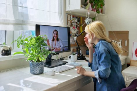 Eine etwa 30 jährige Frau sitzt vor einem Monitor und spricht mit einer Ärztin per Videochat.