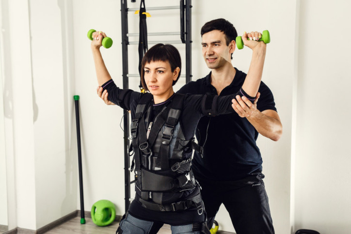 Ein Trainer hilft einer Frau bei EMS-Training-Übungen