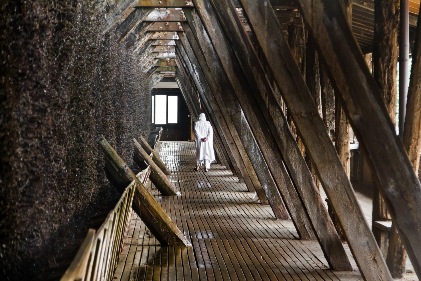 Eine Person im weißen Solemantel spaziert einen Wandelweg im Gradierwerk entlang.