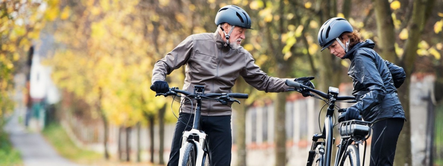 Ein etwa 60 jähriges Pärchen steht an einer asphaltierten Straße und prüft ihre Fahrräder.