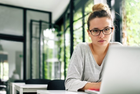 Eine etwa 30-jährige Frau schaut konzentriert auf ihren Laptop.