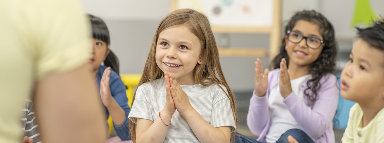Grundschulkinder sitzen im Klassenzimemr auf dem Boden und schauen sich begeistert ein Theaterstück an.