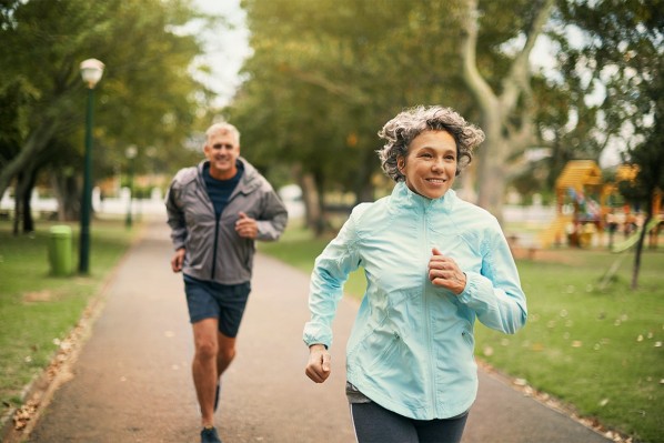 Ehepaar mittleren Alters geht gemeinsam joggen. Sie laufen durch einen Park. 