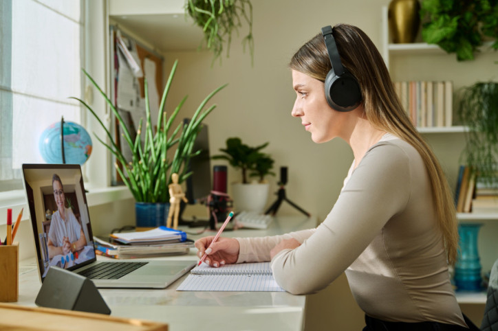 Eine junge Frau nimmt zuhause an einem medizinischem Online-Seminar teil und macht sich dabei Notizen.