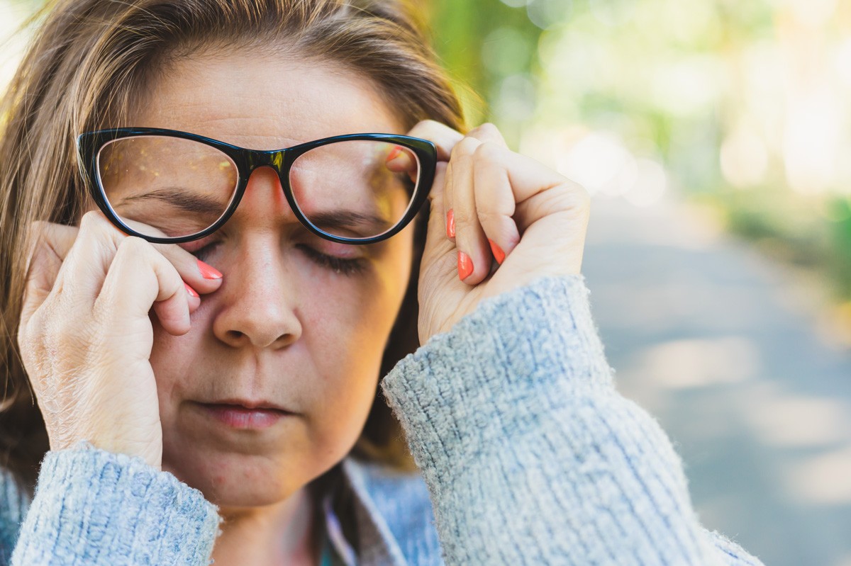 Eine etwa 50-jährige Frau reibt sich ihr Auge, während sie ihre Brille anhebt.