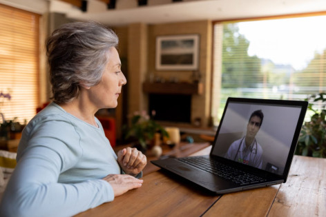 Eine etwa 60-jährige Frau sitzt am Tisch, schaut auf ihren Laptop und hört einem Arzt vom Unimedizin Halle-Talk zu.