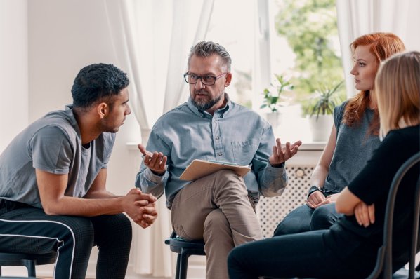 Ein Psychologe sitzt mit drei Jungen menschen bei einer Gruppentherapiesitzung zusammen