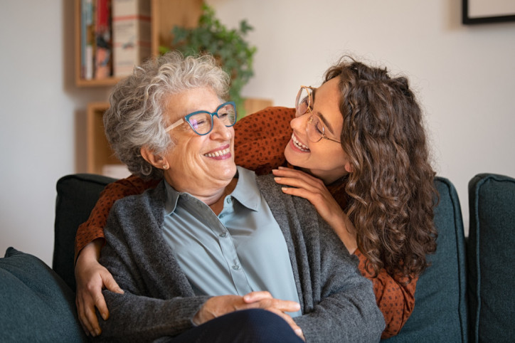 Eine junge Frau schaut eine Seniorin lächelnd über die Schulter an.