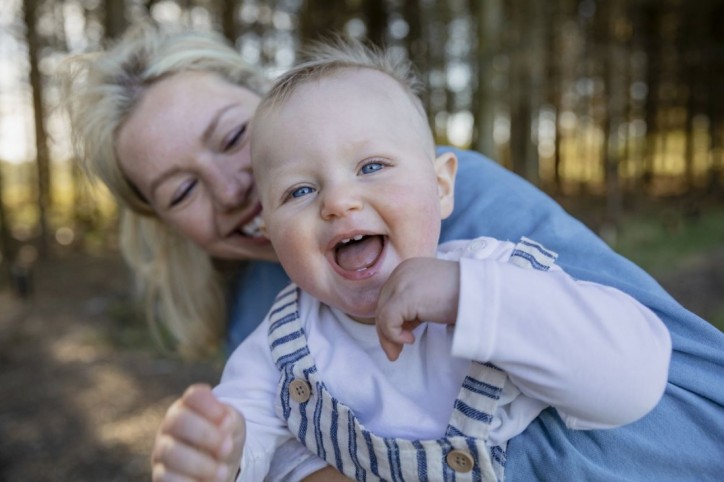 Ein Baby lacht mit seiner Mutter in die Kamera.