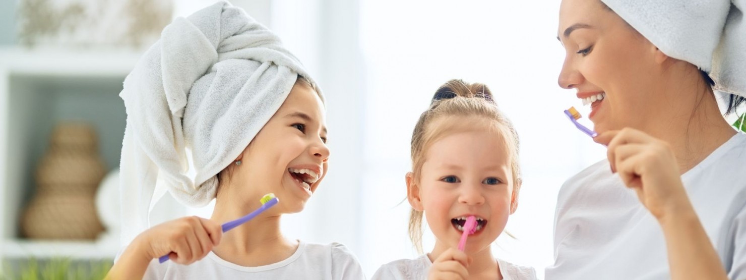 Eine Mutter putzt mit ihren zwei Töchtern die Zähne. Die Frau und das größere Mädchen haben Handtücher um ihren Kopf gewickelt.