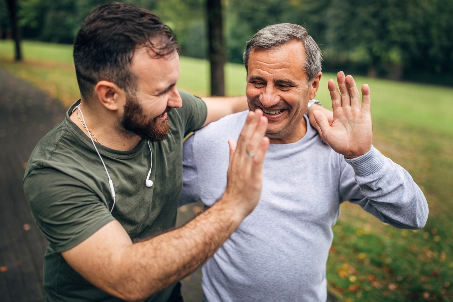 ein Mann ende 30 und ein mann anfang 60 klatschen nach erfolgreichem Lauftraining im park ab