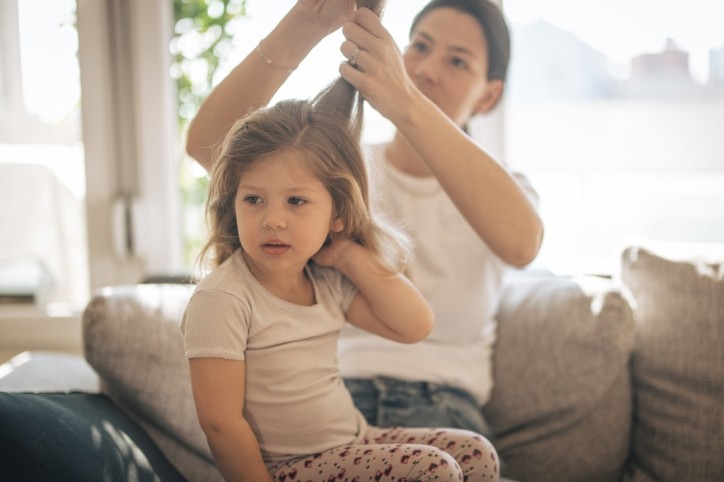 Eine Mutter sucht das Haar ihrer kleinen Tochter nach Zecken ab.