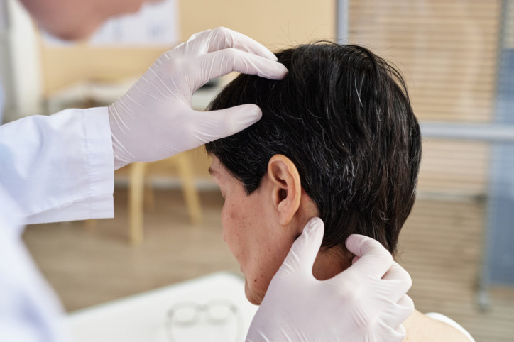 Ein Arzt untersucht die juckende Kopfhaut einer Patientin.