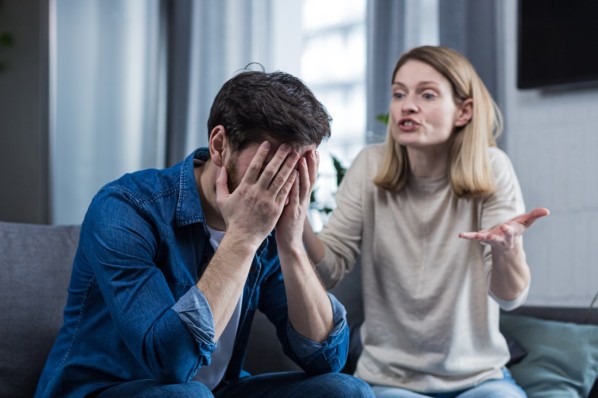 Junges Pärchen sitzt auf der Couch Ihres Wohnzimmers. Der Mann wird von seiner Frau getröstet. 