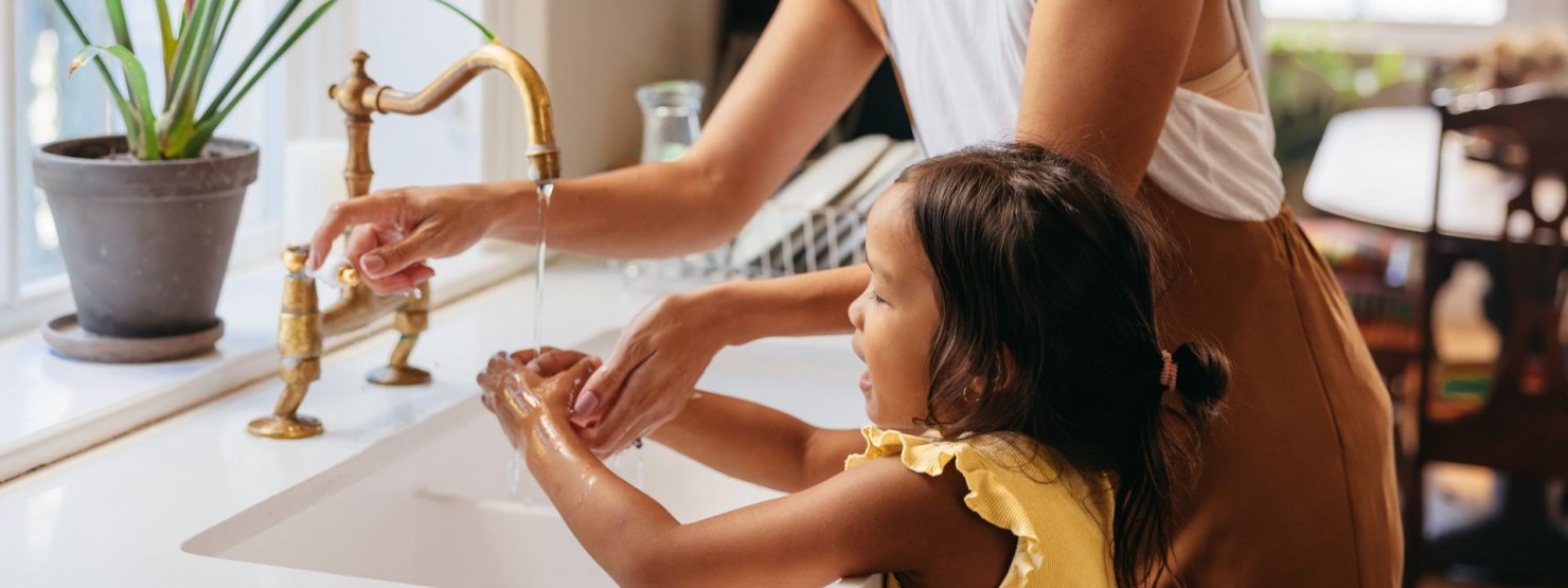 Eine etwa 30 jährige Frau steht mit ihrer kleinen Tochter am Waschbecken und wäscht sich die Hände. 