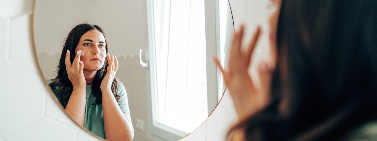 Eine etwa 25-jährige Frau cremt sich ihre Milien an den Augen ein.