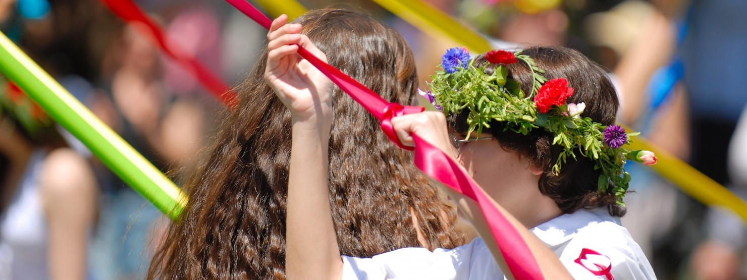 Mädchen mit Blumenkranz im Haar hält Bänder eines Maibaums.