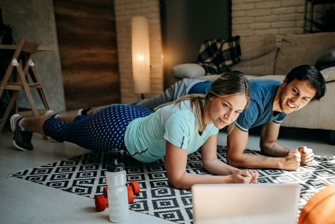 Ein etwa 25 jähriges Pärchen macht gemeinsam Unterarmstütz. Gleichzeitig schauen Sie auf einen Laptop.