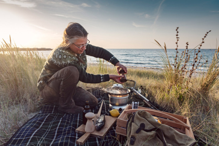 Eine Frau bereitet Fisch nach nordischer Diät am Strand zu 