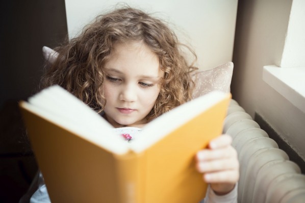 ca 7 jähriges Mädchen mit Locken liest in einem gelben Buch