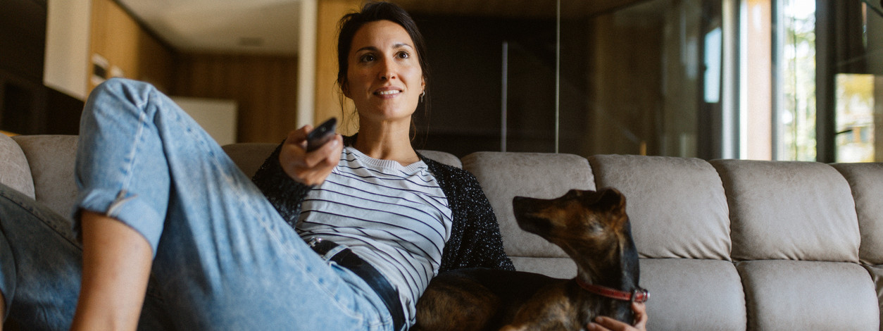 Frau schaut mit ihrem Hund zu Hause fern