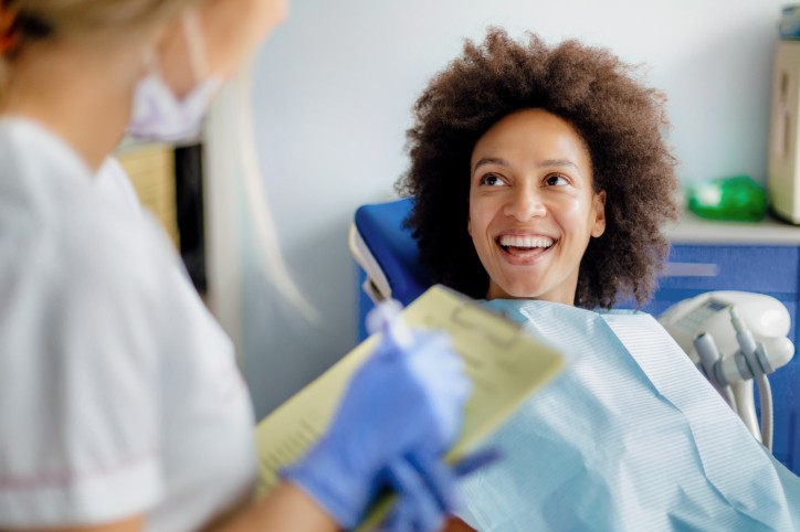 Eine etwa 35-jährige Frau sitzt auf einem Zahnarztstuhl und lächelt ihre Ärztin an.